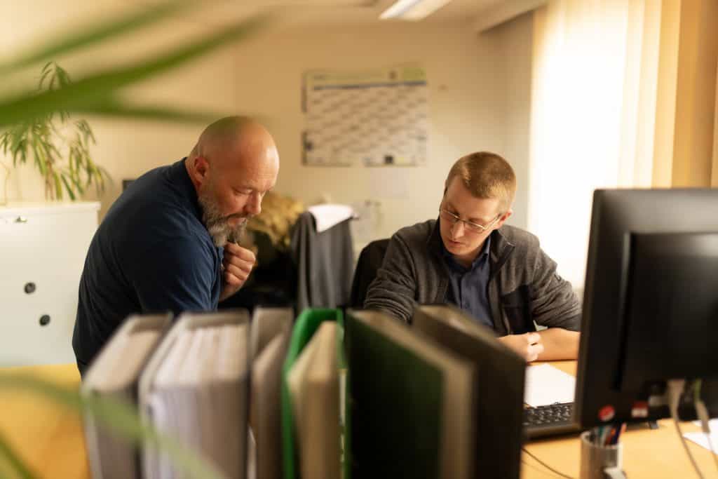zwei Mitarbeiter vom Ingenieurbüro IBOS sitzen am Schreibtisch und schauen konzentriert auf ein Blatt auf dem Tisch.