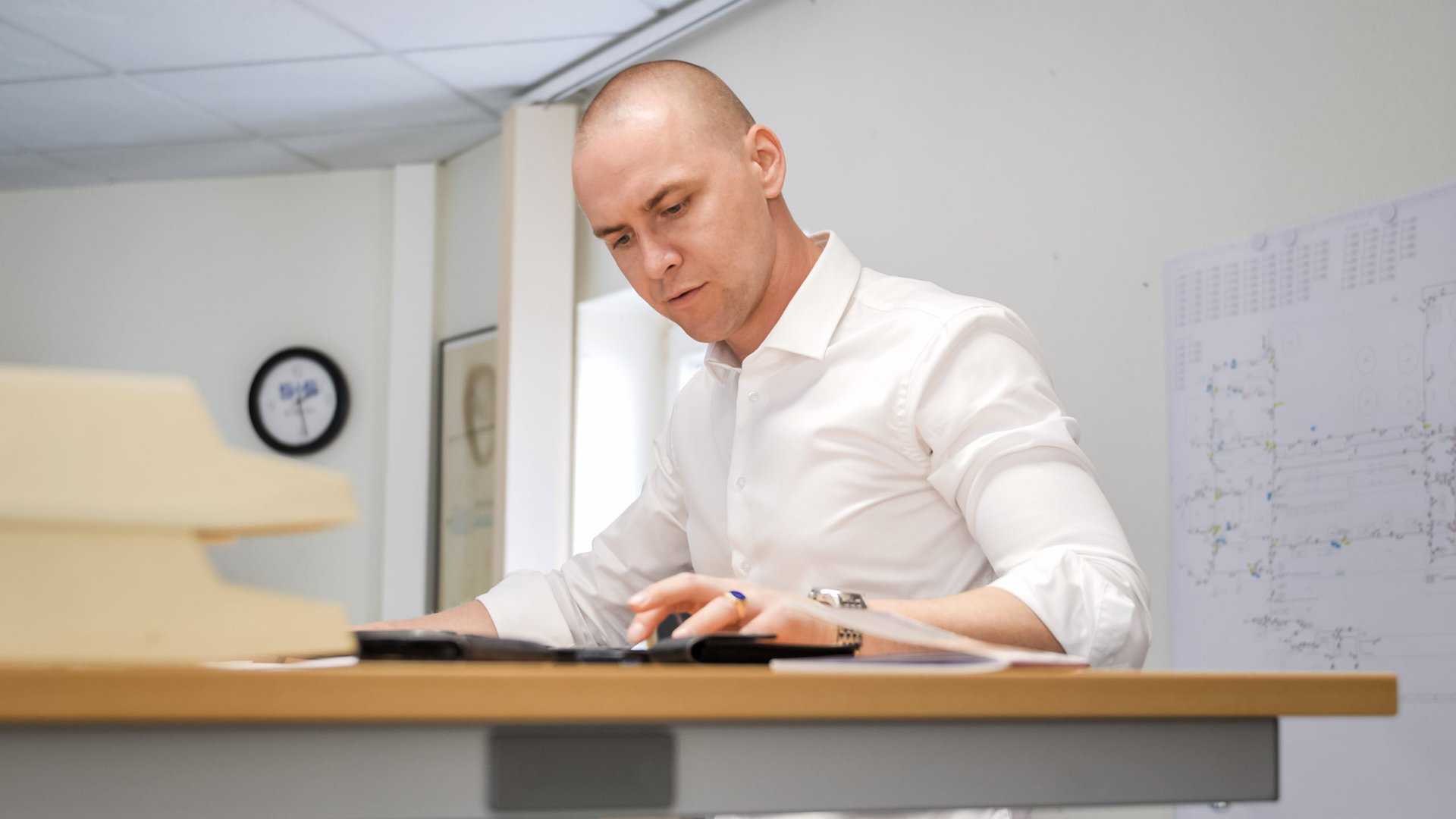 Ein Mitarbeiter berechnet an seinem Schreibtisch Aufgaben mit seinem Taschenrechner